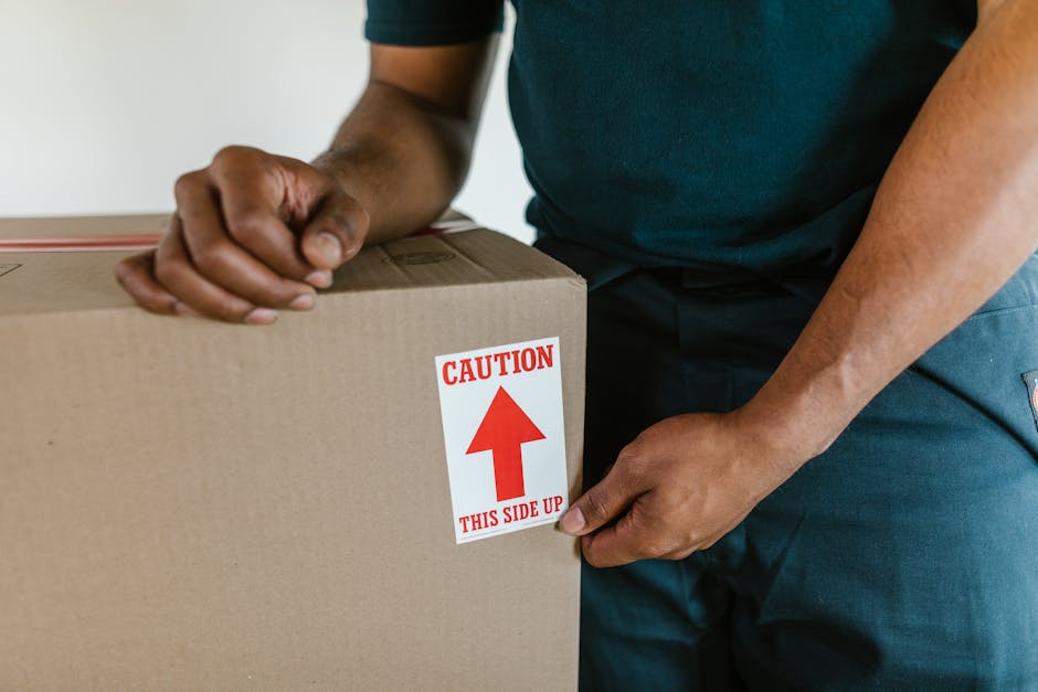 Close-up view of two stacked cardboard boxes in a home interior, with the top box labeled 'STUFF' and featuring a small smiley face drawn in red marker, and the bottom box labeled 'CLOTHES' in black m
