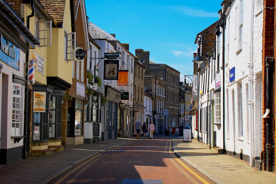 A large, historic brick building with ornate architectural details and a clock on its façade is situated at the centre of a busy marketplace on Roehampton High Street. The scene includes a spacious p